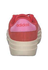 Crvene nubuk tenisice s ružičastim detaljima, s kružnim logotipom, debelim kremastim potplatom i vezicama provučenim kroz rupice na gornjem dijelu.