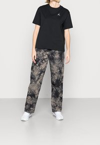 Sort bomulds T-shirt med et lille logo på brystet, parret med løse, tie-dye bukser i nuancer af beige og sort, samt hvide sneakers.
