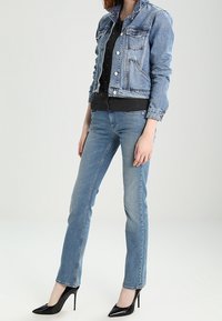 Jeansowa kurtka z srebrnymi guzikami, w jasnoniebieskim kolorze, dopasowany fason; zestawiona z czarną bluzką i wąskimi niebieskimi dżinsami, dopełniona czarnymi szpilkami.