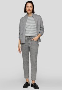 Grauer Cardigan mit Stehkragen, kombiniert mit einem grau gestreiften Oberteil und grauen Jeans. Schwarze Slipper runden das Outfit ab. Flache und strukturierte Stile.