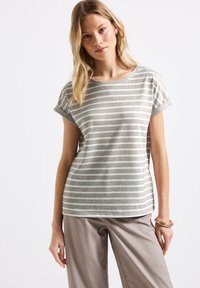 Grå randig kortärmad t-shirt med rundad halsringning och uppvikt ärm, i kombination med ljusbeige byxor. Slät tygets textur.