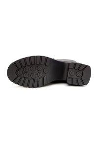 Semelle de chaussure en caoutchouc noir avec un motif de bande de roulement profond et rainuré, comportant des boutons de préhension circulaires, avec une finition lisse et une légère courbure.