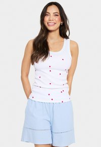 Top blanco sin mangas con estampados de corazones rojos dispersos, combinado con pantalones cortos azul claro con una cintura fruncida y costuras decorativas.