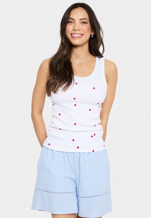 Witte tanktop met verspreide rode hartjesafdrukken, gecombineerd met lichtblauwe shorts met een smockband en decoratieve stiksels.
