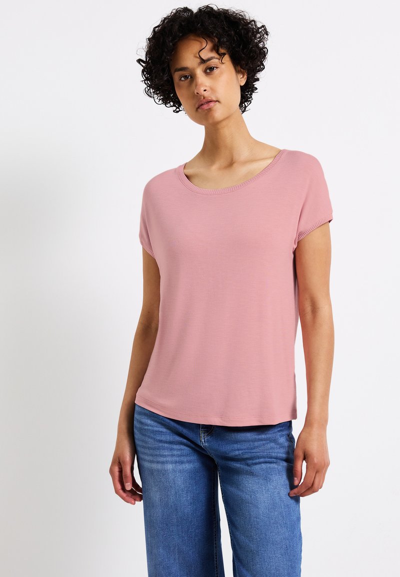 Světle růžové tričko s krátkým rukávem, širokým kulatým výstřihem a měkkou tkaninou, spárované s modrými džíny pro neformální vzhled.