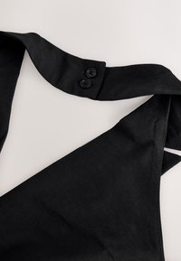 Bandeau en tissu noir avec deux boutons noirs à une extrémité, présenté sur une surface gris clair.