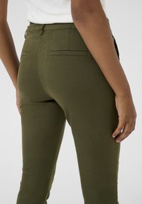 Pantalon ajusté vert olive avec une finition texturée, doté de poches arrière et d'une taille mi-haute, conçu pour une apparence sur mesure.