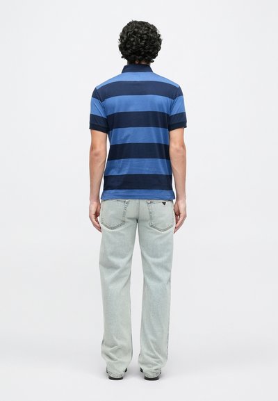 Πόλο μπλούζα με κοντά μανίκια, σε μπλε ναυτικό και ανοιχτό γαλάζιο οριζόντιες ρίγες, συνδυασμένη με ανοιχτόχρωμα, άνετα τζιν παντελόνια, προβολή από πίσω.