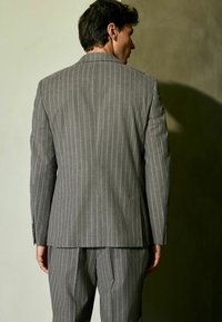 Gray pinstripe suit made of a textured fabric. The jacket features a notched collar and a single vent at the back. Tailored fit and matching trousers.