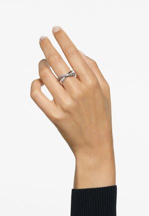 Eine Hand, die einen eleganten silbernen Ring mit einem gewundenen Design und kleinen Edelsteinen trägt, und so Eleganz und modernen Schmuckstil präsentiert.