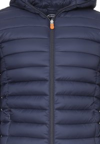 Giacca invernale blu navy con cappuccio, presenta un motivo a righe quiltate orizzontali, chiusura con zip dotata di un linguetta arancione e polsini elasticizzati.