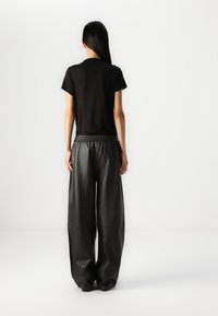 Zwarte t-shirt met korte mouwen en een relaxte pasvorm, gecombineerd met losse zwarte leren broeken met een elastische tailleband en een zachte textuur.