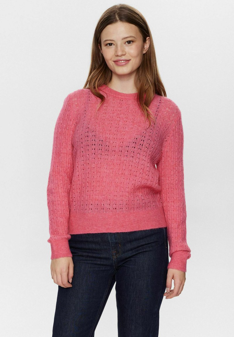 Maglione rosa lavorato a maglia con un motivo testurizzato, scollo rotondo e maniche lunghe. Abbinato a jeans in denim scuro.