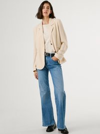 Beige kavaj med lös passform, enkel knappstängning, kombinerad med ljusblå utsvängda jeans. Svart bälte och kraftiga svarta skor fulländar looken.