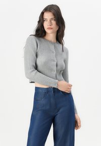Šedý žebrovaný zkrácený cardigan s kulatým výstřihem a předním zapínáním na knoflíky. Ve spojení s modrými džíny s vysokým pasem.