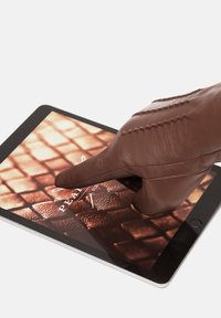 Smeđa kožna rukavica dodiruje zaslon tableta koji prikazuje teksturirani uzorak. Tablet ima srebrni okvir s crnim rubom zaslona.