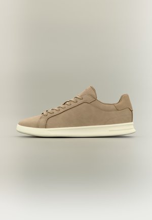 Baskets basses beige avec semelle blanche, laçage frontal, finition mate lisse et col rembourré, présentées de profil sur un fond neutre.