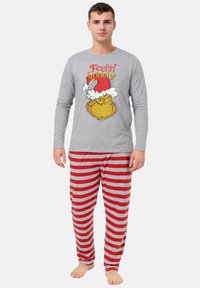 Maglietta da pigiama a maniche lunghe grigia con la scritta "Feelin' Grinchy" e grafica del Grinch in stile cartoon. Pantaloni da pigiama a righe rosse e grigie. Materiale in cotone morbido.