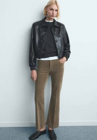 Giacca di pelle nera, maglione grigio, camicia bianca e pantaloni a zampa di cotone a coste marroni. Scarpe slip-on nere completano il look.