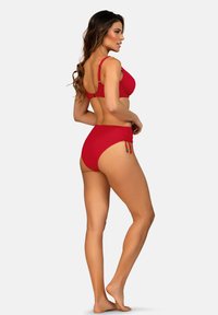 Czerwony komplet bikini z usztywnionym stanikiem na regulowanych ramiączkach oraz majtkami z wysokim stanem, ozdobionymi marszczeniem i wiązaniami po bokach. Gładka faktura tkaniny.
