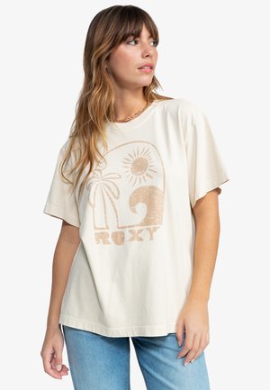 Beige oversize póló, textúrált grafikával, amelyen nap, pálmafa és hullám látható; rövidujjú és laza fazonú.