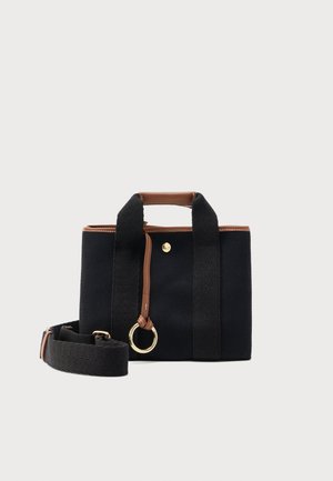 Bolsa tote de tela negra con detalles en cuero marrón, asas cortas, correa ancha para el hombro desmontable y un llavero en forma de anillo dorado.