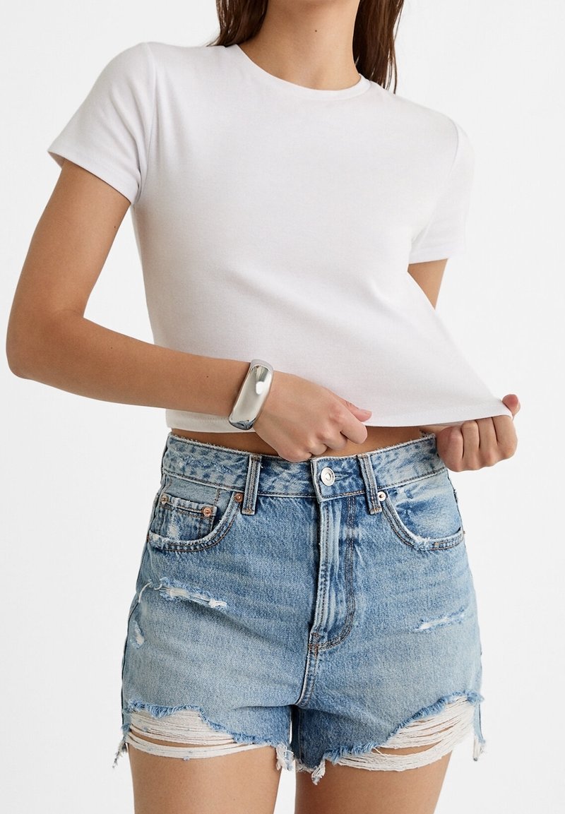 T-shirt blanc en coton à manches courtes associé à un short en denim bleu, présentant un ourlet effiloché et des bords frangés, mettant en avant un look décontracté.