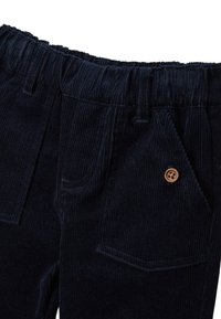 Pantalons en velours côtelé bleu marine avec une taille élastique, présentant des poches avant et un détail de bouton marron. Le tissu texturé et côtelé est visible.