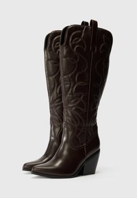 Bottes de cowboy en cuir marron avec un bout pointu, des motifs de feuilles brodés, un talon haut effilé et des tirettes en haut.