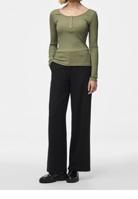 Olivově zelený top s dlouhým rukávem, žebrovanou strukturou a knoflíkovými detaily, spárovaný s černými širokými kalhotami a černými botami.