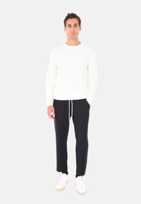 Maglione bianco a coste abbinato a pantaloni neri con coulisse e sneakers bianche con suola beige. Design semplice e silhouette aderente.