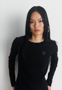 Black long-sleeve shirt made of soft fabric, featuring a small blue circular logo on the chest. Simple design with a fitted silhouette.