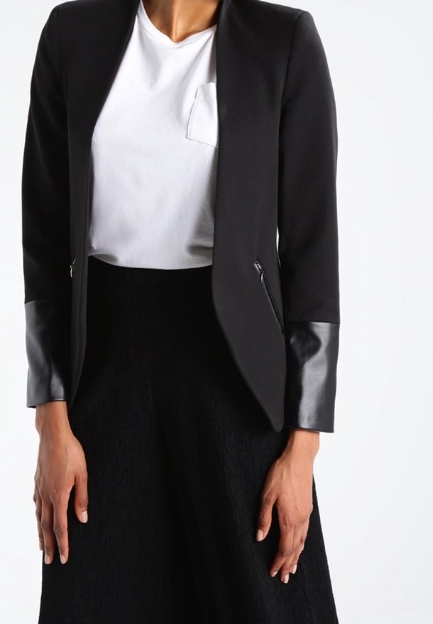 Černé sako s matnými a lesklými koženými rukávy, se zipovými kapsami, nošené přes bílé tričko s malou kapsou na hrudi a černou sukni.