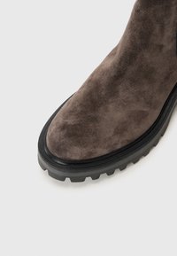 Bottine en daim marron avec un bout arrondi et une semelle en caoutchouc texturé présentant des profondeurs pour une meilleure adhérence. Accent de semelle intermédiaire noire.