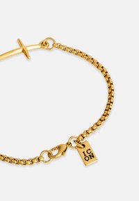 Arany árnyalatú karkötő sima láncvázlattal, homárkapoccsal és "ICON" felirattal gravírozott címkével. A felülete sima és fényes láncokkal rendelkezik.