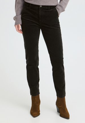 Femme portant un pantalon en velours côtelé noir slim, associé à des bottines en daim marron et un pull gris à manches longues.