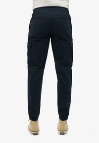 Pantalons cargo bleu marine avec taille élastique, chevilles ajustées et poches latérales. Fabriqués en tissu léger avec une texture lisse.