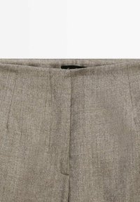 Gros plan d'un pantalon en tissu gris montrant la taille, la couture avant et une fermeture éclair dissimulée.