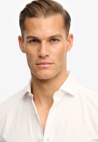 Witte overhemd met knopen, gemaakt van een zachte stof met een lichte glans, met een scherpe kraag en een klein geborduurd logo op de borst.