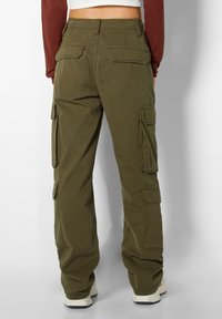Olivengroene cargobroek met een losse pasvorm, meerdere zijzakken en achterzakken. De stof is stevig en heeft zichtbare stiksel details.