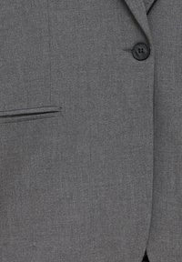 Veste grise avec un seul bouton noir, un revers cranté et une poche horizontale étroite sur le côté gauche.