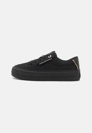 Zapatillas de lona negras con suela de goma negra gruesa, puntera redonda y detalles dorados en la lengüeta y el talón. Presentan cierre de cordones.
