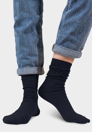 Granatowe skarpetki prążkowane o miękkiej strukturze z marszczoną mankietem, zestawione z podwiniętymi niebieskimi dżinsami.