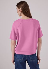 Sweatshirt rose court avec un col rond, des manches raglan et un ourlet légèrement court, associé à un jean en denim bleu.