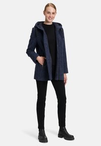 Granatowa, fakturowana kurtka z kapturem, z zapięciem na zamek z przodu i bocznymi kieszeniami, noszona na czarnym topie i czarnych spodniach; masywne czarne buty.