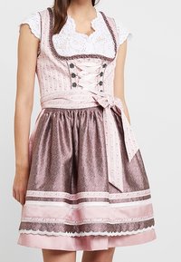 Tradycyjny dirndl w kolorze różowym, z dopasowaną górą z detalami w stylu sznurowania, spódnicą w kwiatowy wzór oraz białymi koronkowymi akcentami przy dekolcie.