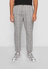 Czarno-białe spodnie w kratę o zwężanym kroju z kieszeniami cargo, wykonane z lekkiego materiału. W zestawie ze srebrnymi sneakersami.