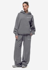 Set di felpa grigia e pantaloni abbinati realizzati in tessuto morbido, con cappuccio e tasca frontale, caratterizzato da dettagli con logo bianco su entrambi i capi.