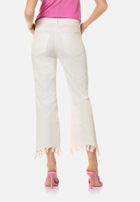 Jeans de pierna ancha de color claro con dobladillos deshilachados y bolsillos traseros, combinados con sandalias de tacón rosa. Textura suave, diseño casual.