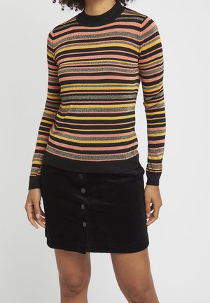 Personne portant un pull à manches longues rayé en noir, rose, jaune et paillettes, assorti d'une jupe en velours côtelé noire à boutons sur le devant.